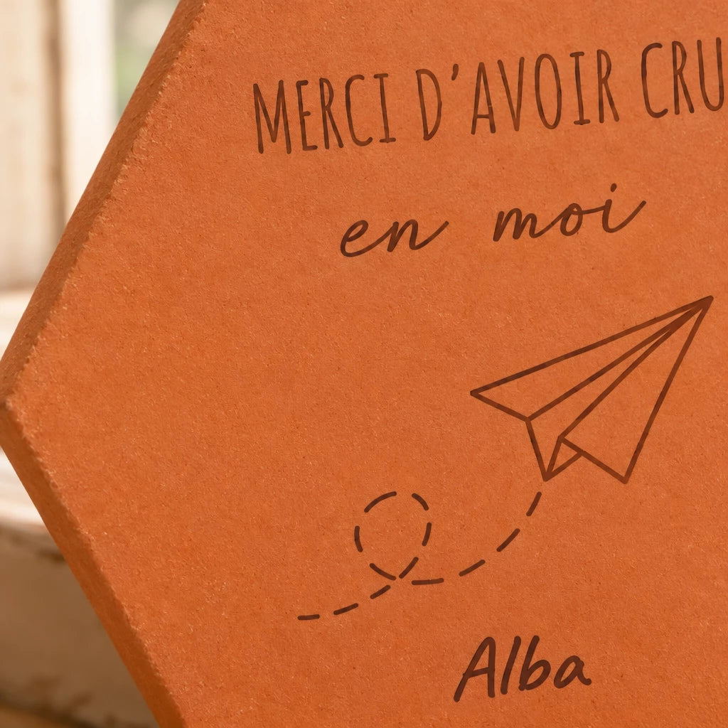 Detalle del grabado láser: «Merci d'avoir cru en moi», el avión de papel, su estela de puntos y el nombre Alba.